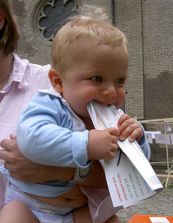 Oskar Vogel beit auf bedrucktes Papier, whrend er auf dem Arm einer nicht zu erkennenden Person gehalten wird. Fotograf unbekannt